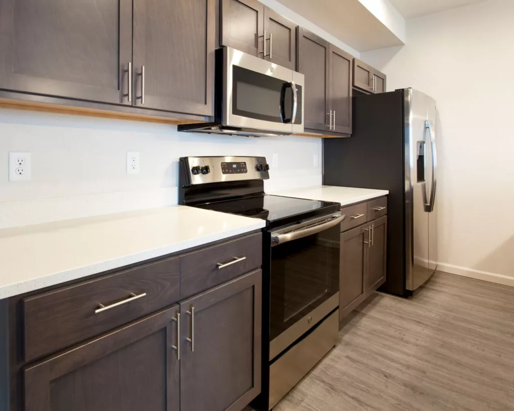 Modern kitchen with stainless steel appliances, including a microwave, oven, and refrigerator, dark wooden cabinets, and light countertops.